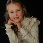 Blond meisje met witte treui voor een donkere achtergrond in een leuke pose