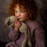 Meisje met rode krullen in mooi zacht licht met haar knuffeltje