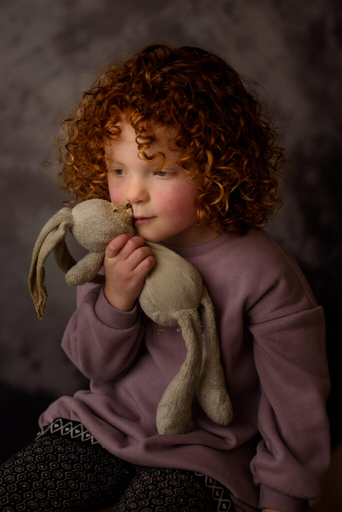 Meisje met rode krullen in mooi zacht licht met haar knuffeltje