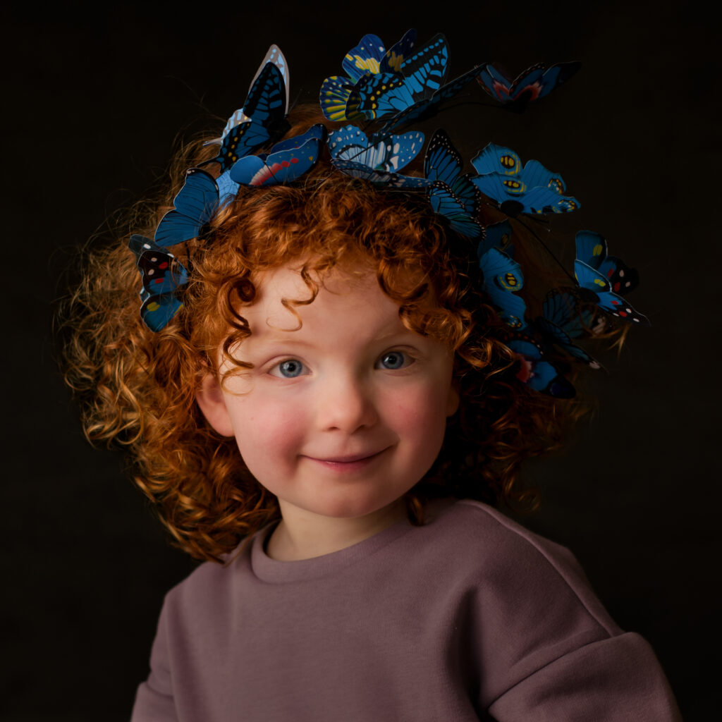 Portret van roodharig meisje met blauwe vlinderkroon in zachte studioverlichting